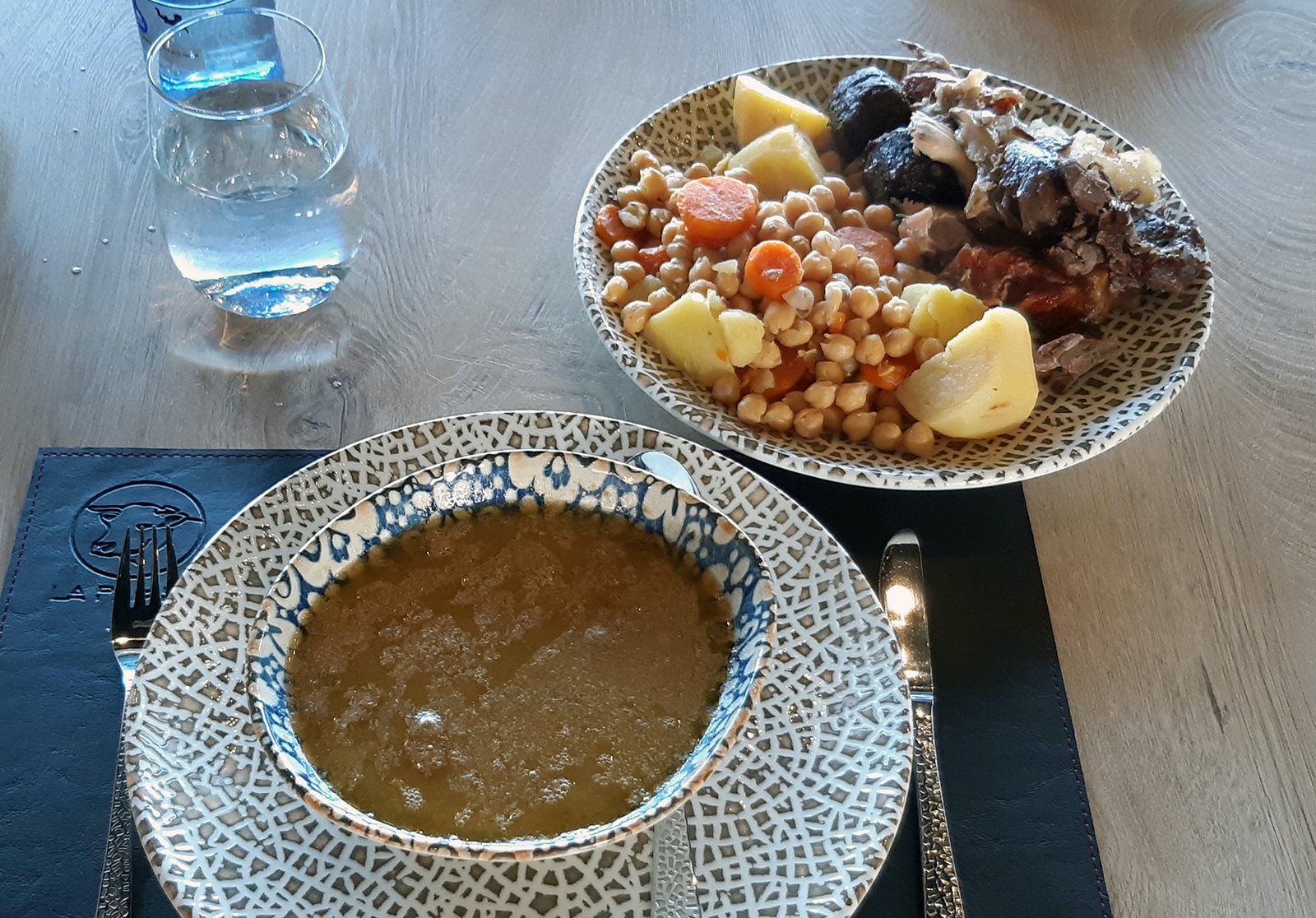 Plato de sopa de cocido junto a garbanzos, verdura, carnes y chorizo